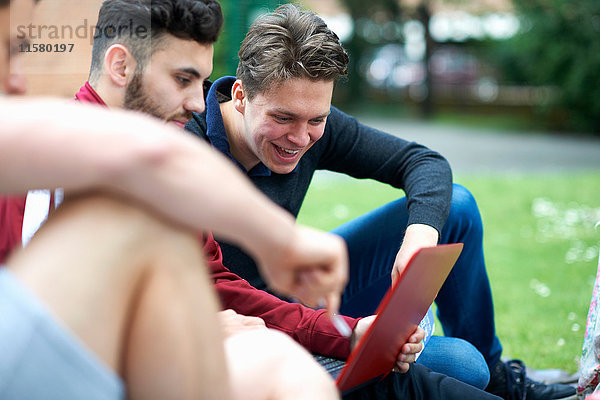 Drei männliche Freunde sitzen im Freien und schauen auf das digitale Tablet