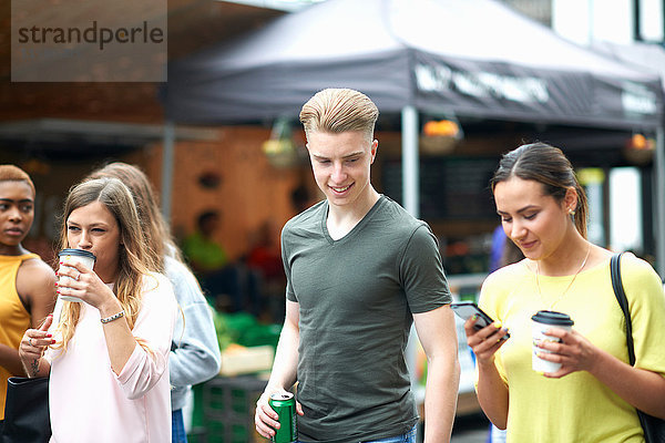 Gruppe von Freunden  Spaziergang im Freien  Getränke tragen  Smartphone anschauen