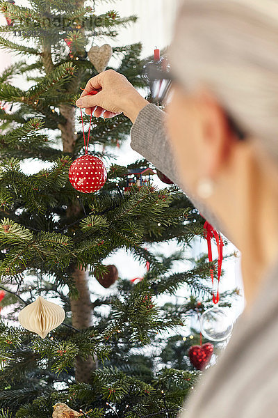 Ältere Frau legt Christbaumkugel auf Weihnachtsbaum