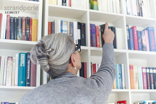 Ältere Frau nimmt Buch aus dem Bücherregal  Rückansicht