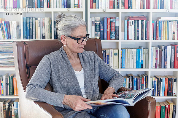 Ältere Frau sitzt auf einem Stuhl in der Bibliothek und liest ein Buch