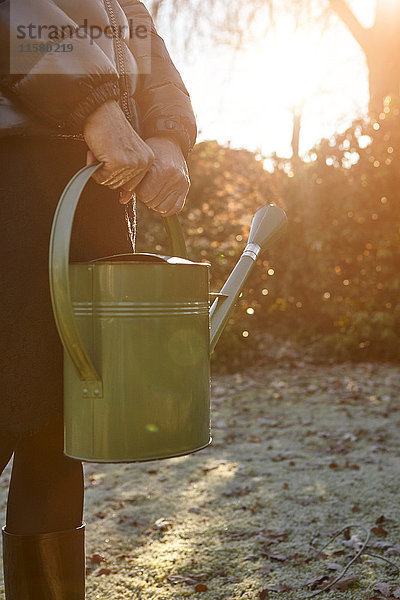 Ältere Frau steht im Garten  hält Giesskanne  Mittelteil