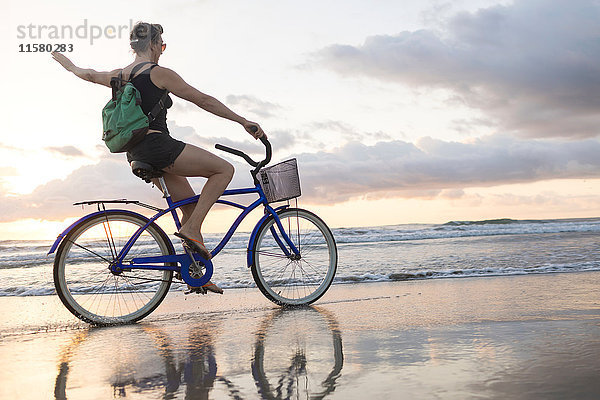Frau winkt beim Radfahren am Strand bei Sonnenuntergang  Nosara  Provinz Guanacaste  Costa Rica