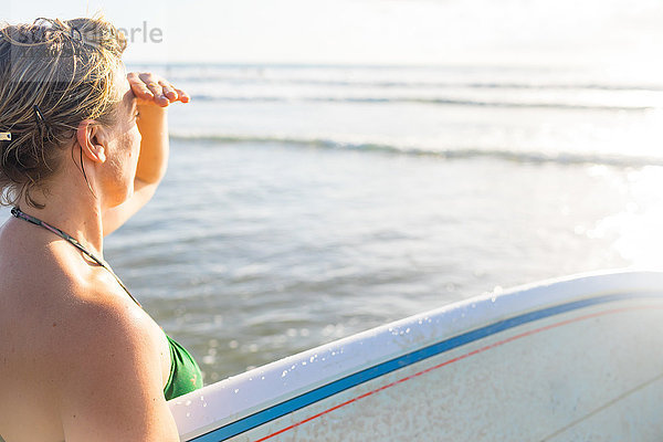 Frau trägt ein Surfbrett und schaut vom Strand aufs Meer hinaus  Nosara  Provinz Guanacaste  Costa Rica