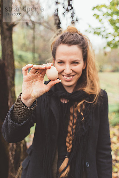 Junge Frau hält Ei im Garten