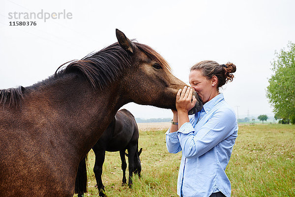 Frau mit dem Gesicht zur Pferdeschnauze im Feld