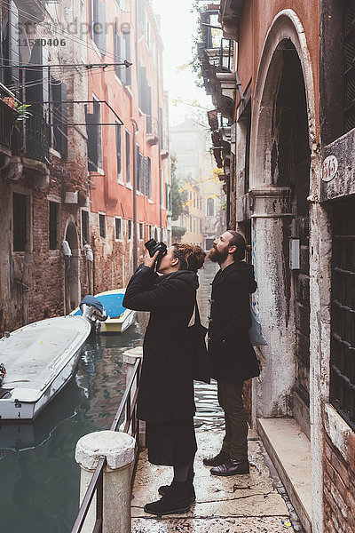 Ehepaar fotografiert Gebäudeaußenseiten vom Kanalufer aus  Venedig  Italien