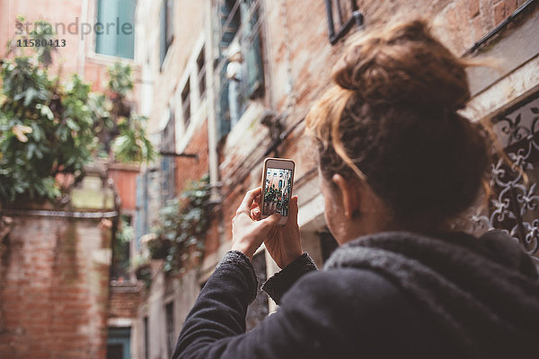 Über-die-Schulter-Ansicht einer Frau  die Gebäude mit einem Smartphone fotografiert  Venedig  Italien