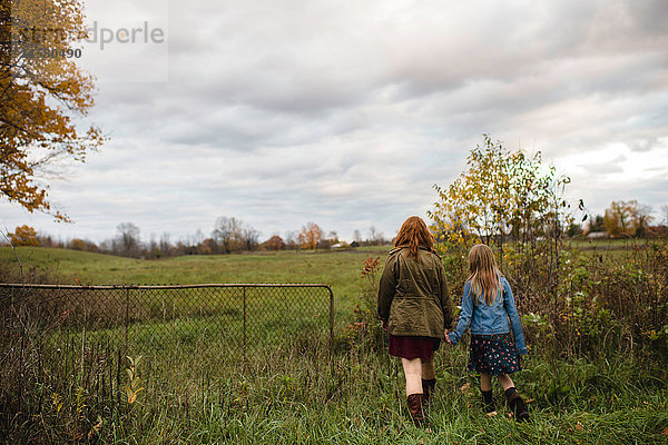 Mutter und Tochter halten sich beim Spaziergang auf einer Wiese an den Händen  Lakefield  Ontario  Kanada