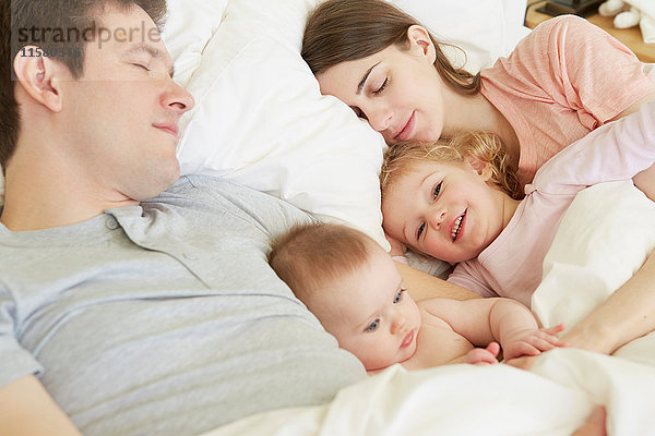 Mädchen und Schwester im Kleinkindalter kauern mit schlafenden Eltern im Bett