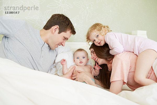 Weibliches Kleinkind und kleine Schwester spielen mit den Eltern im Bett