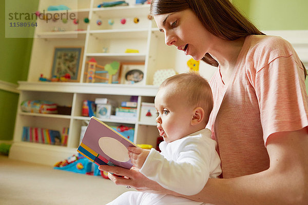 Mittelgroße erwachsene Frau und kleine Tochter lesen Märchenbuch im Spielzimmer