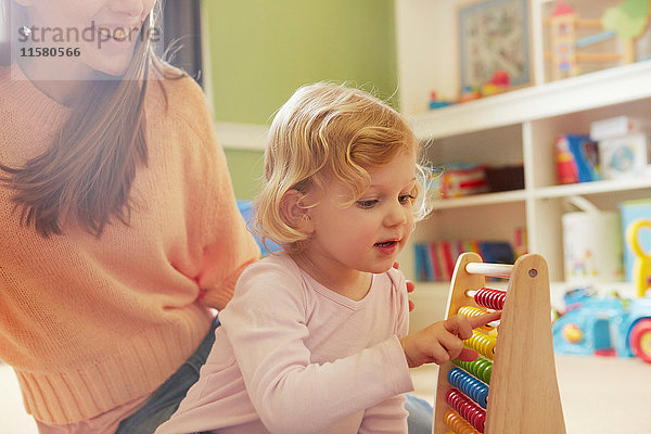 Mittlere erwachsene Frau und Kleinkind-Tochter rechnen mit Abakus im Spielzimmer
