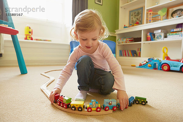 Weibliches Kleinkind spielt mit Spielzeugeisenbahn auf dem Boden des Spielzimmers