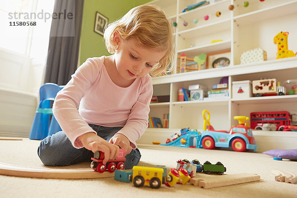 Weibliches Kleinkind spielt mit Spielzeugeisenbahn auf dem Boden des Spielzimmers