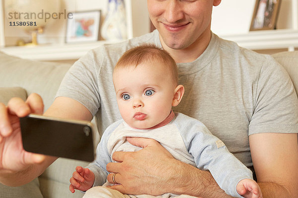 Mittelgroßer erwachsener Mann nimmt Smartphone-Selfie mit Baby-Tochter auf Sofa