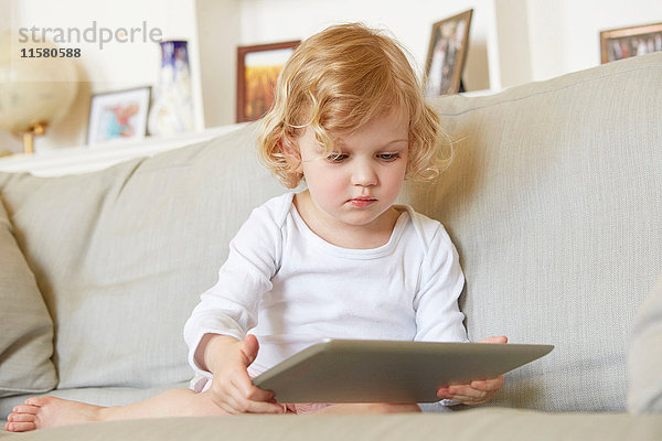 Weibliches Kleinkind sitzt auf dem Sofa und benutzt ein digitales Tablett