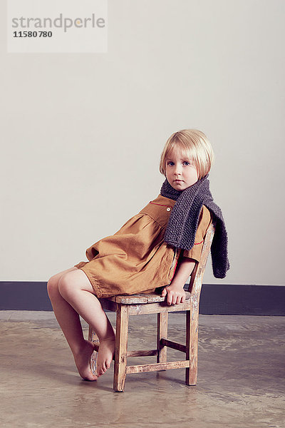Porträt eines mürrischen Mädchens  das auf einem alten Holzstuhl sitzt.