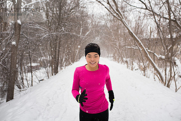 Glückliche junge Läuferin mit Strickmütze läuft in einem von Bäumen gesäumten  schneebedeckten Park
