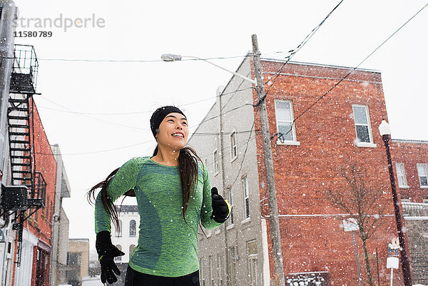 Glückliche junge Läuferin mit Strickmütze läuft auf verschneiter Straße