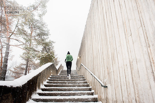 Rückansicht einer jungen Läuferin mit Strickmütze  die eine schneebedeckte Treppe hinaufläuft