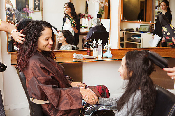Mädchen und Mutter halten sich an den Händen  während ihr Haar im Friseursalon gestylt wird.