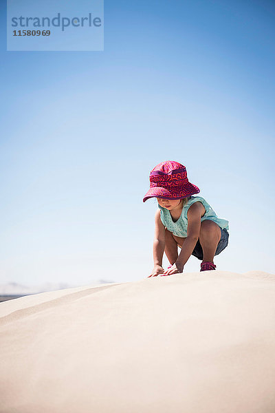 Weibliches Kleinkind kauert auf der Spitze einer Sanddüne  Little Sahara  Utah  USA