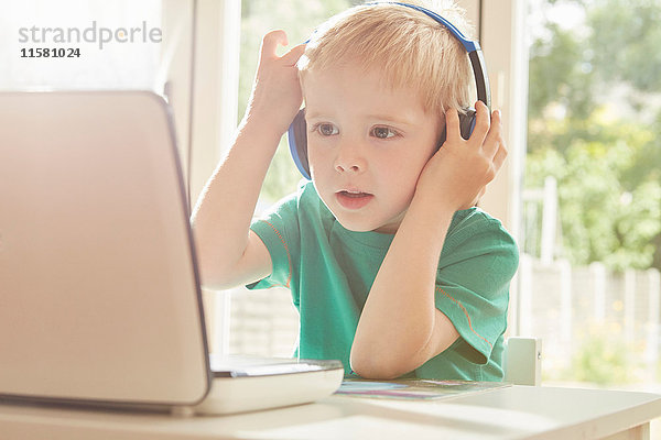 Junge am Schreibtisch mit Laptop und Kopfhörern