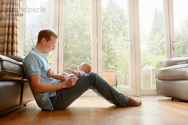 Reifer Mann sitzt auf dem Boden mit einem kleinen Sohn auf dem Schoß