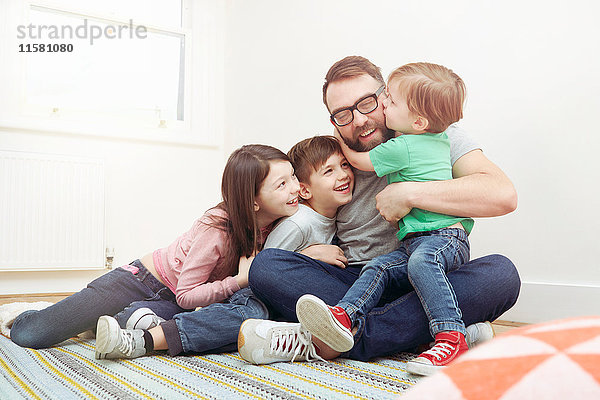 Ein mittelgroßer Erwachsener und drei Kinder sitzen auf dem Boden und umarmen sich
