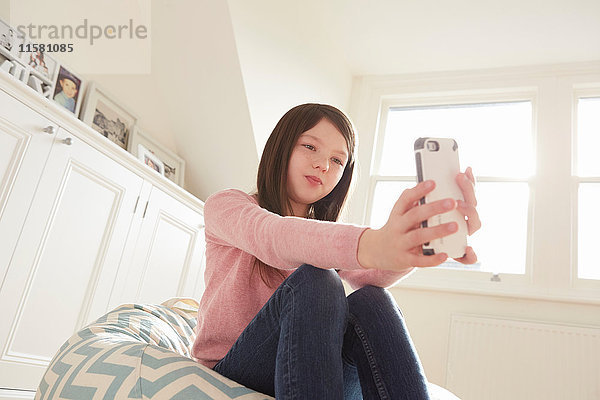 Mädchen sitzt auf Sitzsackstuhl und nimmt Smartphone-Selfie