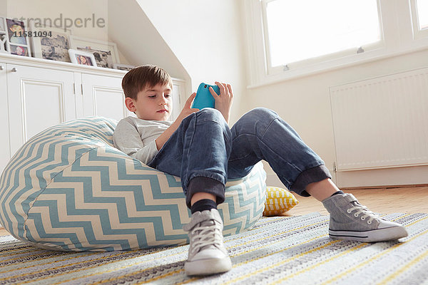 Auf Sitzsackstuhl liegender Junge betrachtet digitales Tablett