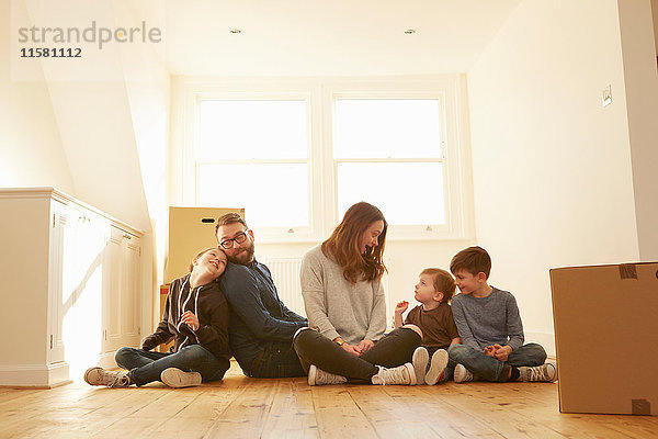 Mittleres erwachsenes Paar und drei Kinder sitzen auf dem Boden in einem neuen Heim.