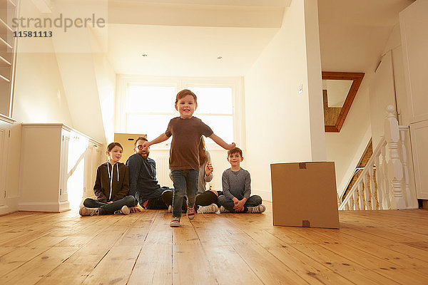 Porträt eines männlichen Kleinkindes und einer Familie  die auf dem Boden in einem neuen Zuhause sitzen.