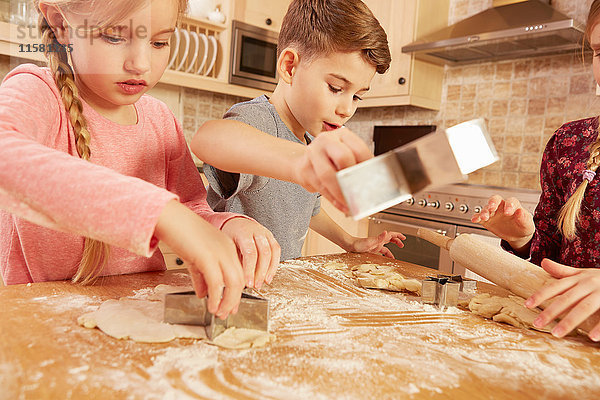 Mädchen und Jungen backen sternförmiges Gebäck am Küchentisch