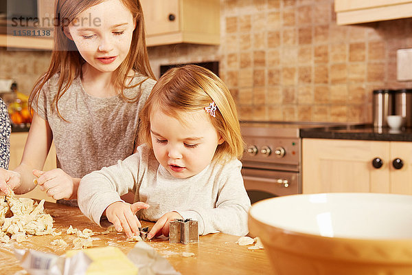 Weibliches Kleinkind und große Schwester machen sternförmiges Gebäck am Küchentisch