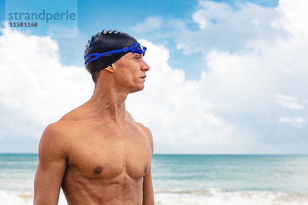 Muskulöser männlicher Schwimmer am Strand  der wegschaut