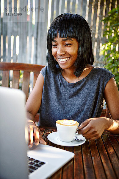Junge Frau sitzt im Freien  benutzt Laptop  trinkt Kaffee