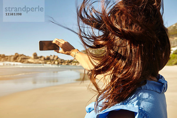 Reife Frau am Strand  Selfie  Smartphone benutzen  Rückansicht