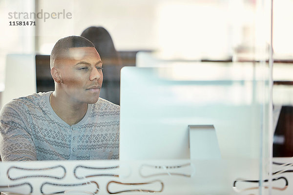 Universitätsstudent arbeitet am Computer hinter einer Glastrennwand