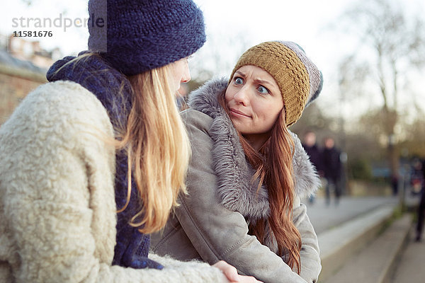 Zwei Freundinnen im Freien  auf Stufen sitzend  herumalbernd  Gesichter ziehend