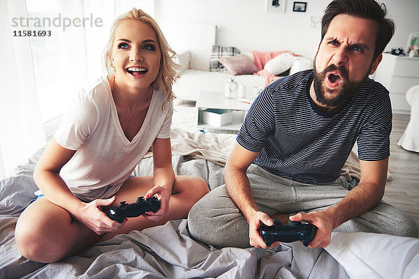 Paar sitzt auf dem Bett  hält Computer-Controller in der Hand  spielt Computerspiel