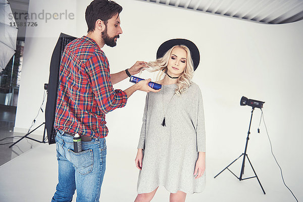 Männlicher Fotograf  der die Haare eines weiblichen Modells auf studio-weißem Hintergrund einstellt