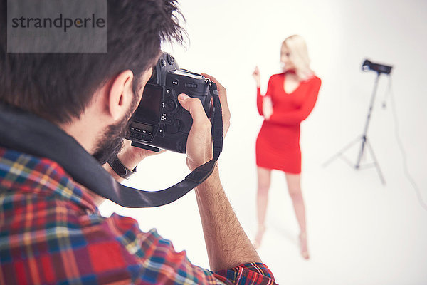 Über-Schulter-Ansicht eines männlichen Fotografen  der ein weibliches Modell auf studio-weißem Hintergrund fotografiert