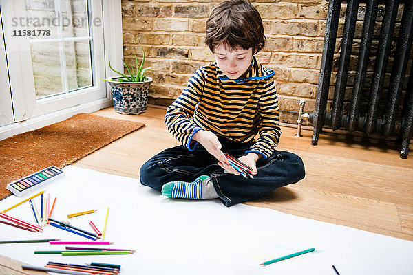 Auf dem Boden sitzender Junge zeichnet auf langem Papier