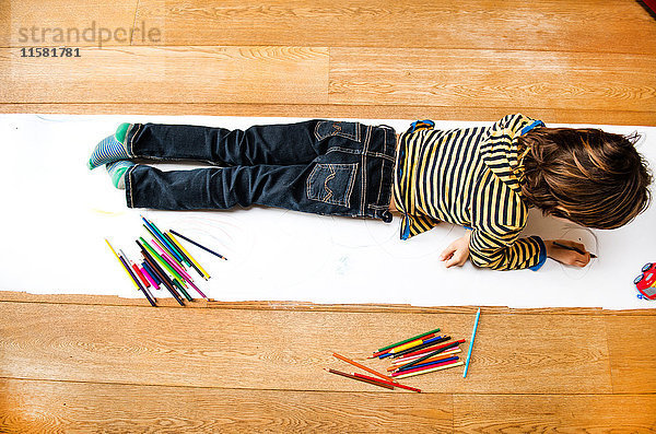 Draufsicht eines Jungen  der auf einem langen Papier liegt und zeichnet