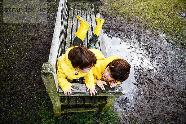Draufsicht auf den kleinen Jungen und Bruder in gelben Anoraks auf der Parkbank