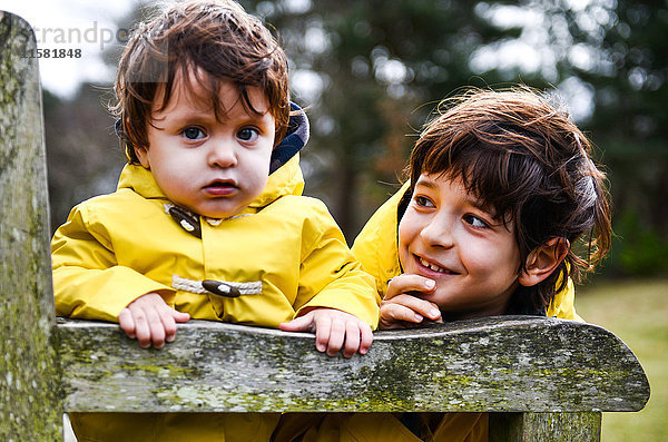 Porträt eines kleinen Jungen und eines großen Bruders in gelben Anoraks auf einer Parkbank