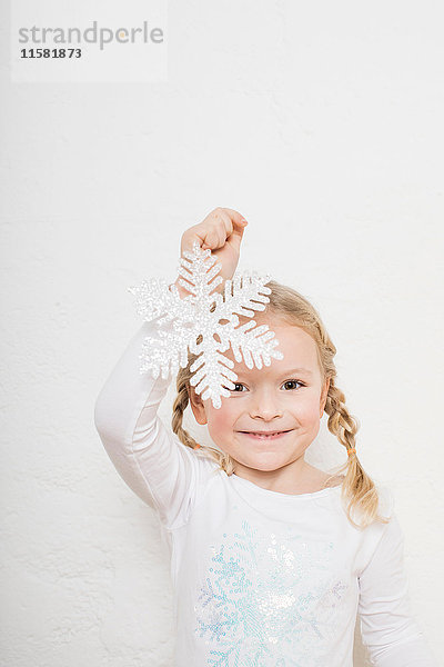 Porträt eines jungen Mädchens vor weißem Hintergrund  das eine Schneeflocke hält