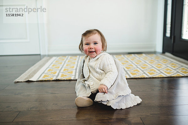 Rosarotes Baby sitzt lächelnd auf dem Boden